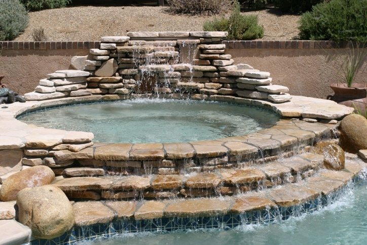 A round spa edged in stacked flagstone, spilling over a stone waterfall into a pool.